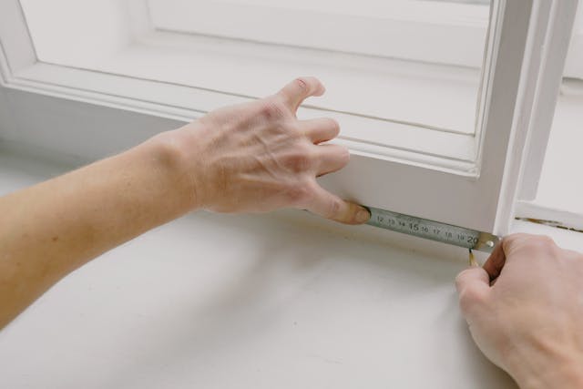 hands using a tape measure on a window frame